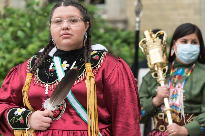 Kaeliana Smoke, wearing Indigenous regalia, carries an eagle feather ahead of the convocation mace bearer.