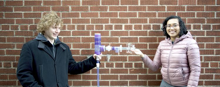 Austin Mclean and Rashmi Satharakulasinghe stand on either side of a plastic spigot which has a long spout with valves.