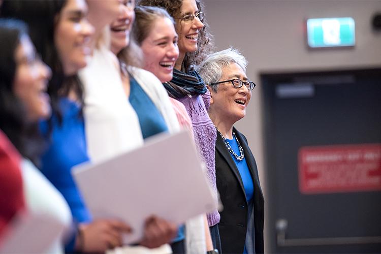 Carol Chin and five other women smile broadly as they sing together.
