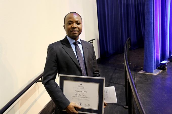 Suleyman Demi on the stage ramp at Convocation Hall, smiling and holding his Gordon Cressy Student Leadership Award