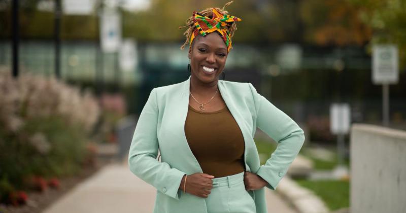 Desiree Kaunda-Wint  smiles, standing with hand on hip on a walkway outdoors.