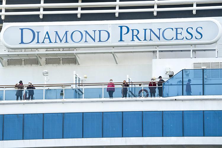 Masked people stand on the deck of a cruise ship under a banner that reads Diamond Princess.