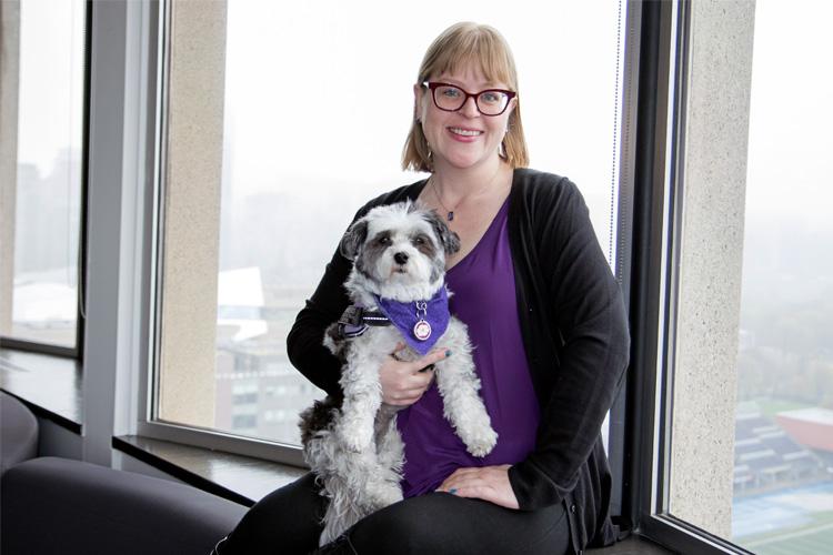 Emaily Wright smiles and holds her service dog Kailey, as they sit in a window seat overlooking Toronto.