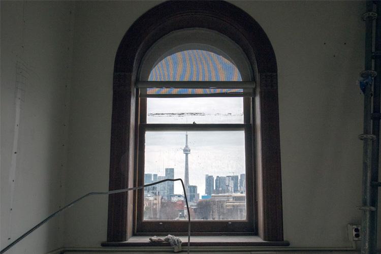 A window in an empty room shows a view of the CN Tower and Toronto Islands
