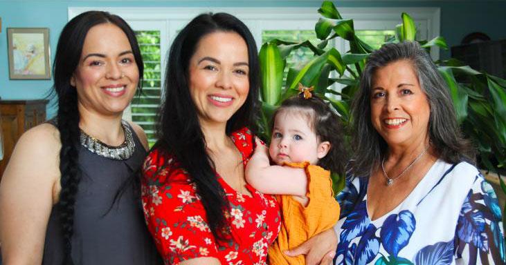 Cynthia Wesley-Esquimaux smiles as she stands next to her two daughters. One daughter holds her own small daughter.