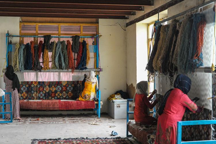 Women work in pairs on giant looms weaving elaborate carpets in a Kabul workshop.