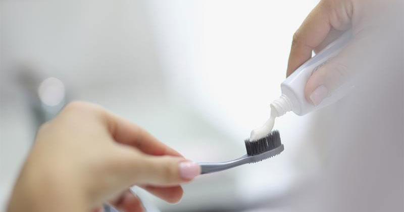 A close-up of a person's hands as they squeeze toothpaste onto a toothbrush.