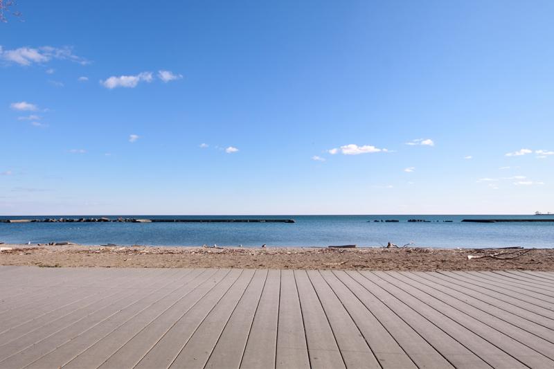 An empty beach, with a flat horizon, sparkling lake, straight waterline and a boardwalk made of flat straight boards.