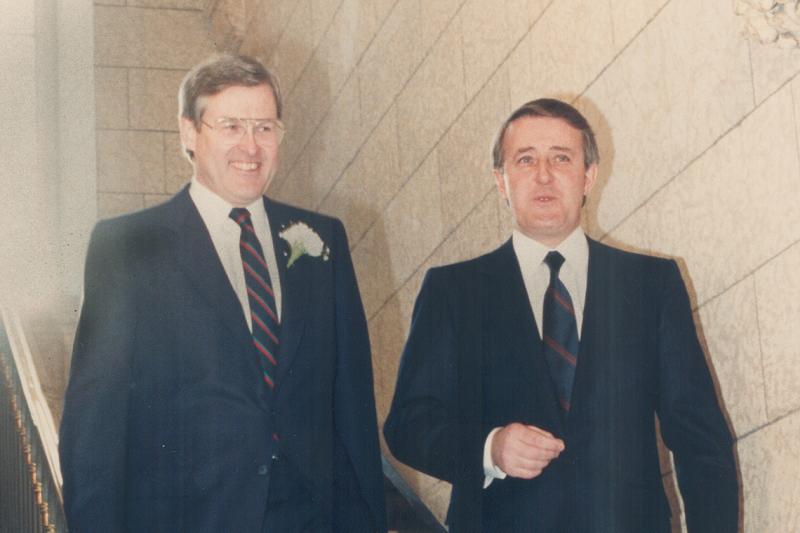 In an old photo from 1986, Michael Wilson and Brian Mulroney chat and smile while walking down a staircase.