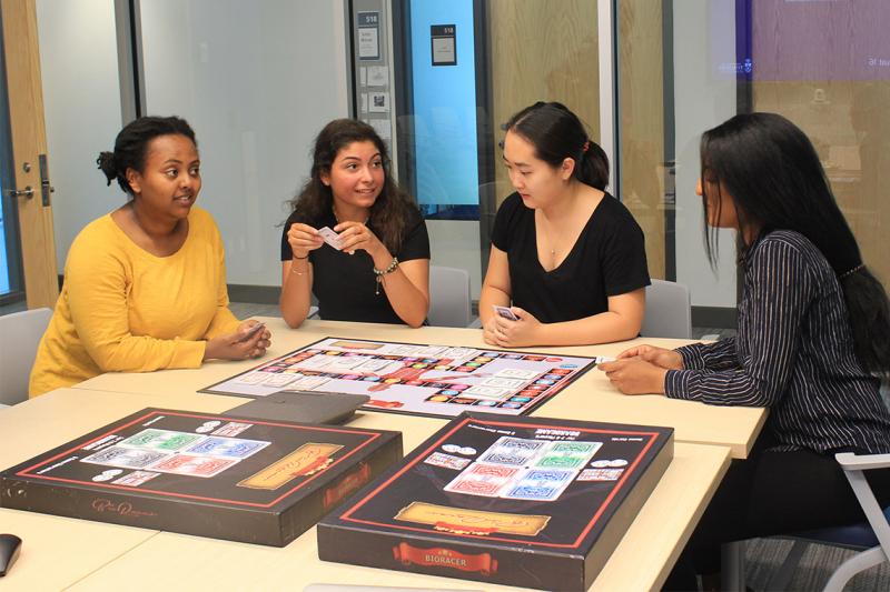 Four students chat as they sit around a table laid out with a board game.