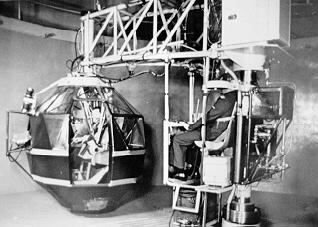A large device has a circular pod on a crane that can be whirled around a central post. The pod fits one person.