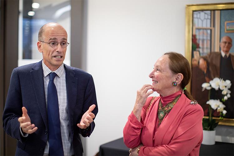 Edward Iacobucci gestures while Rosalie Abella looks on, smiling, at a party indoors.