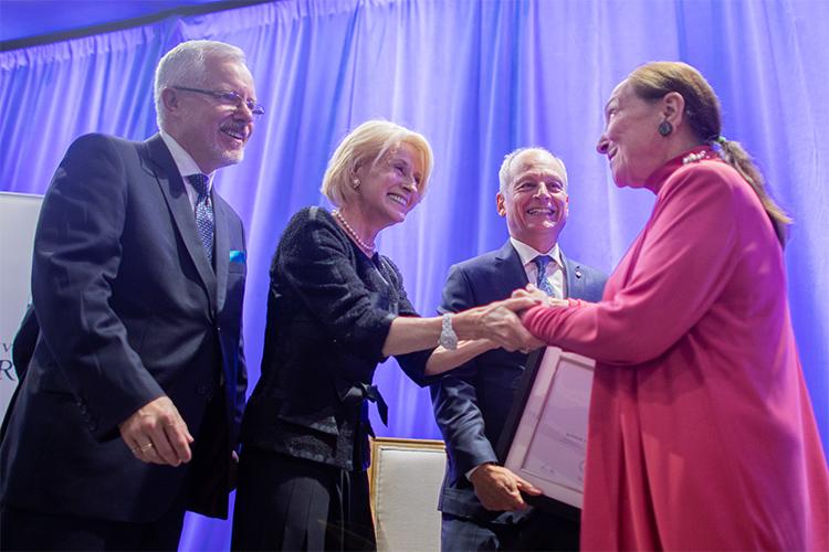 Beaming, Rose Patten clasps hands with Rosalie Abella as Scott MacKendrick and Meric Gertler look on, smiling.