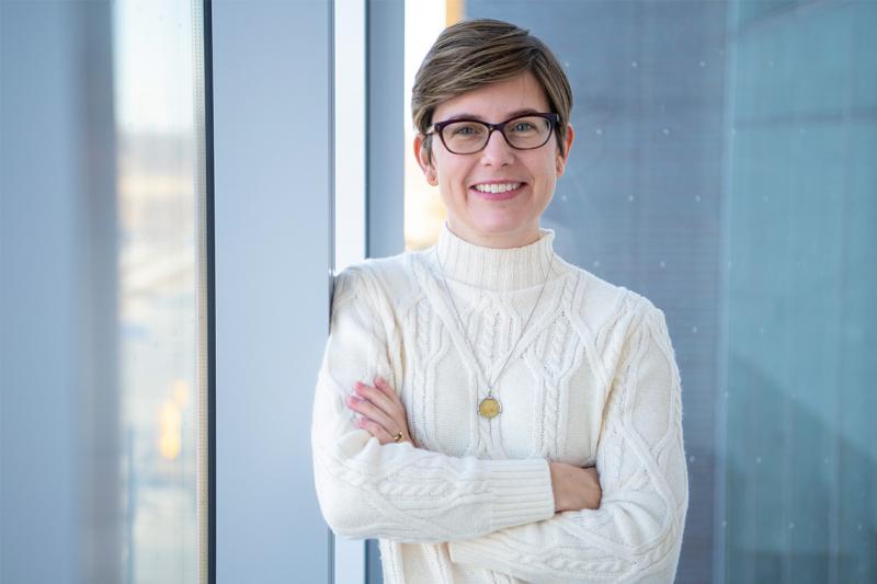 Karen Smith smiles, leaning on a glass wall and crossing her arms.