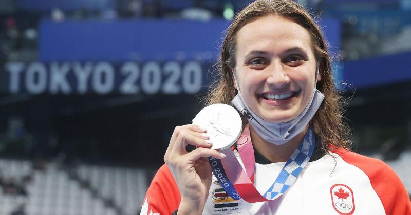 Kylie Masse smiles as she holds up her Olympic silver medal. A banner behind her reads: Tokyo 2020.