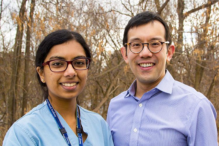 Kirusanthy Kaneshwaran and Andrew Lim smile, standing outdoors in a wooded area in winter.