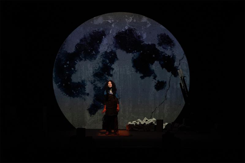 An actress on stage with a picture of the moon behind her