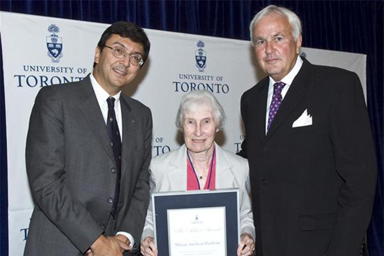 Marian Packham holds her framed Arbor Award as she stands between two university officials at a presentation.