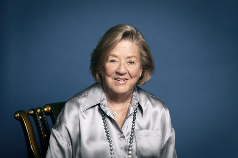 Margaret McCain sits smiling against a blue background.