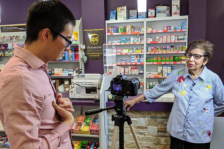 Michael Do interviews a pharmacist, who stands in front of a shelf of pills.