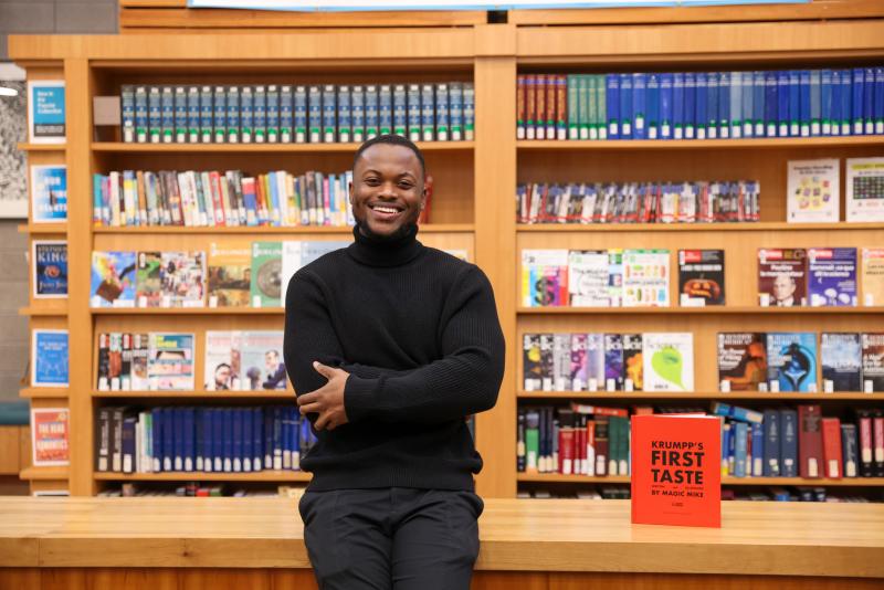 Michael Gayle stands against a table in a library, with his book displayed next to him