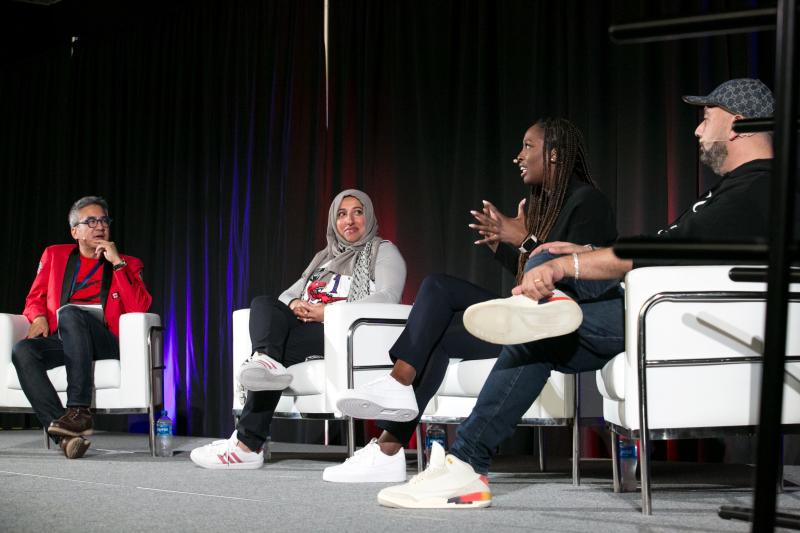 Four people sitting on a stage in white armchairs 