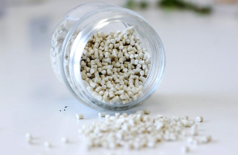 Small pellets of compostable, plant-based resin spill out of a glass jar.