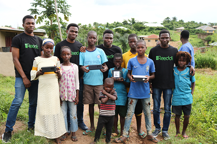 Olugbenga Olubanjo and three friends in Reeddi T-shirts smile with kids holding small portable power cells.