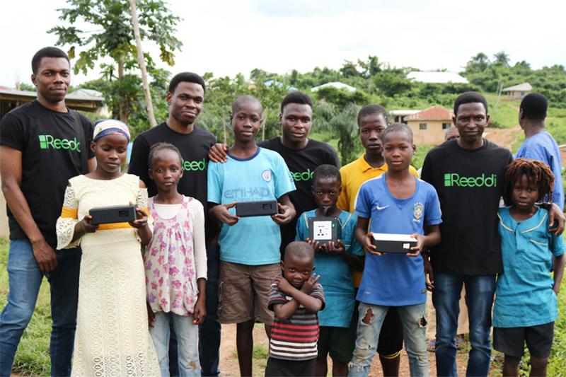 Workers in Reeddi t-shirts, including Olugbenga Olubanjo, stand with children in a rural village.