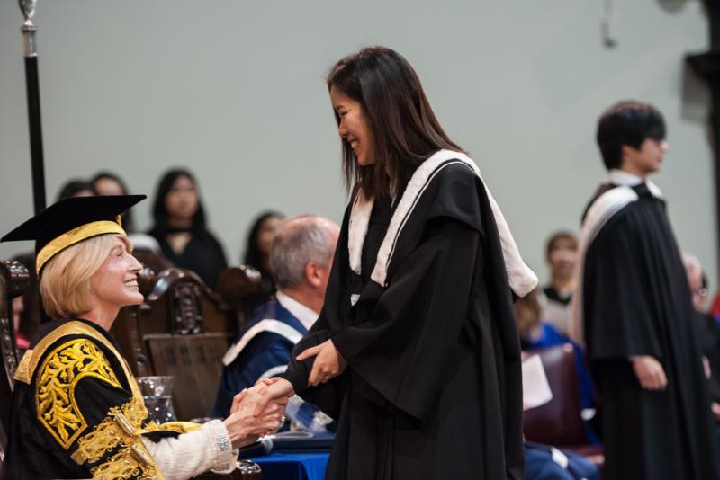 Rose Patten shakes hands with a graduate in U of T's Convocation Hall (photo by Lisa Sakulensky)