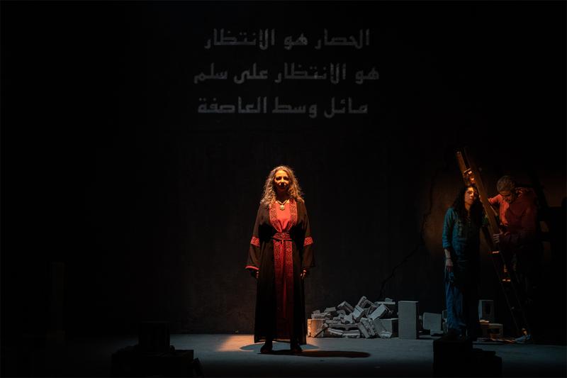 Three actors stand on stage with rubble behind them