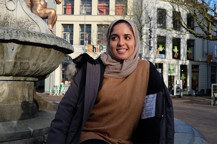 Rowaida Hussein smiles while sitting on the edge of a fountain in an empty city square.