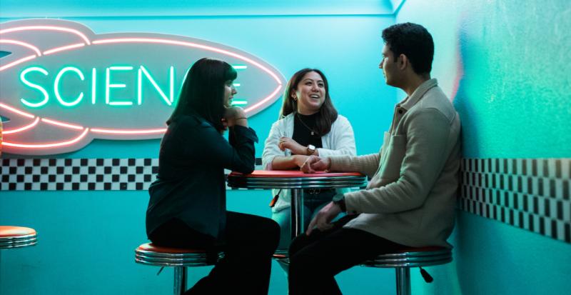 Photo of alumni sitting together chatting in front of a sign that reads science.