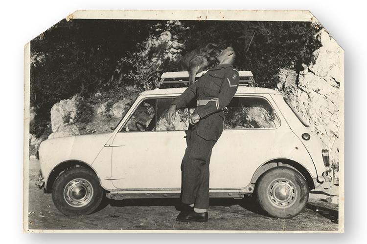 In the 1940s, a monkey on the roof of a car takes food from the mouth of a man in uniform.