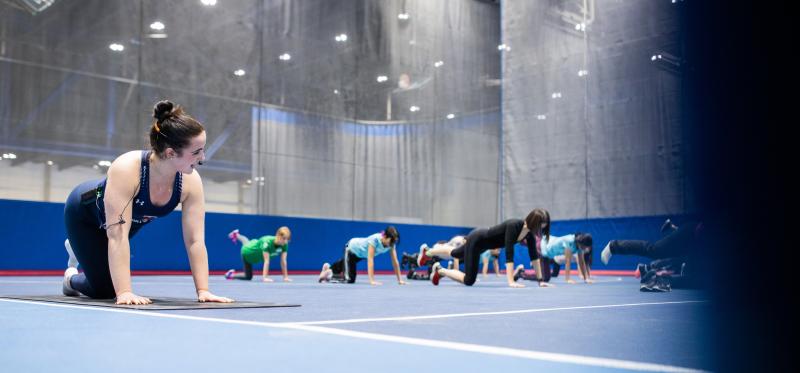 A group of women on yoga mats kneel and stretch out one leg behind them.