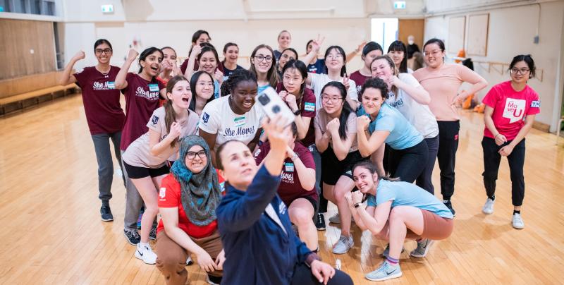 25 women pump their fists and pose for a group selfie.