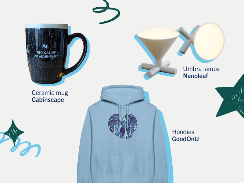 a black ceramic mug with the text "tiny cabin, big adventures", a blue hoodie saying "inclusion is love" and two small carryable conical lamps