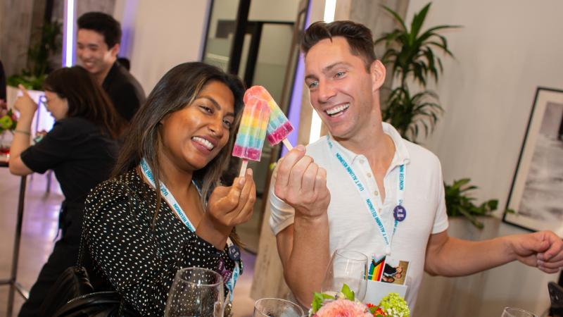 Two alumni holding rainbow popsicles smiling.