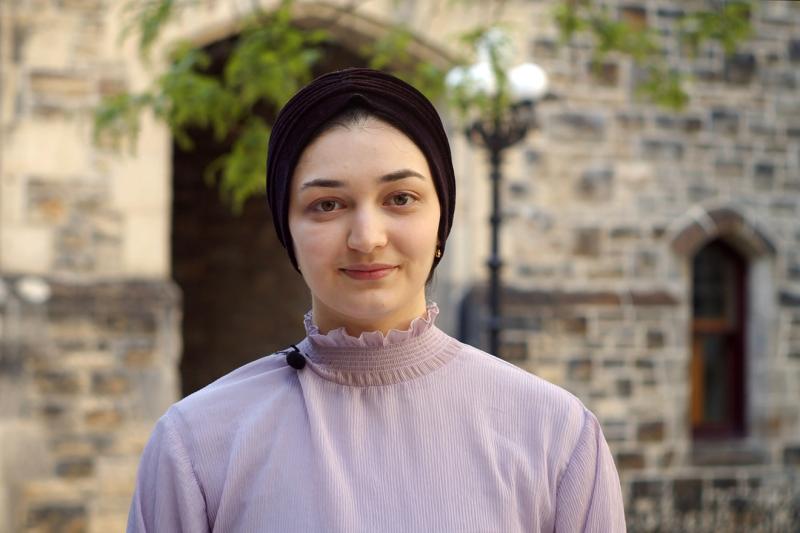 A young woman with a headscarf smiles into the camera