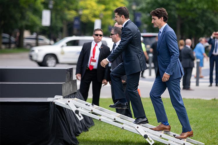 Volodymyr Zelenskyy and Justin Trudeau walk, one after the other, up a makeshift metal staircase to a set of risers before a photo call.