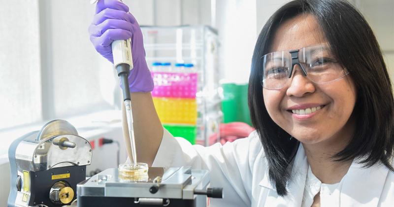 Ruby Sullan, wearing gloves and goggles, smiles as she holds up an eyedropper.