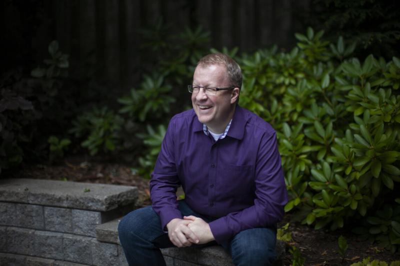 Professor Scott Gray-Owen laughs as he sits on a bench in a garden.