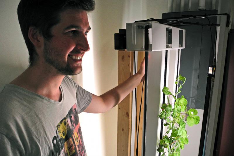 Conner Tidd holds a frame with plants growing out of its vertical sides.