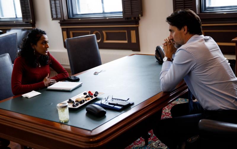 Vandana Fatima Kattar and Justin Trudeau chat, sitting on opposite sides of a table.