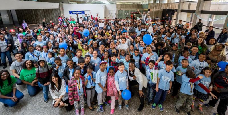 More than 100 kids from all backgrounds pose for a giant group picture, wearing Visions of Science t-shirts.