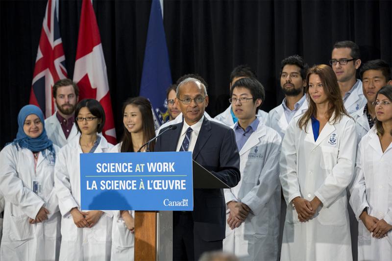 Vivek Goel speaks in 2015. A sign on the podium reads: Science at work. Behind him stand several young doctors in white coats