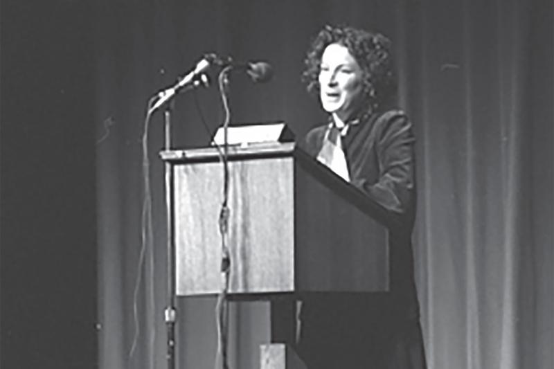 A young Margaret Atwood speaks into a microphone at a podium.