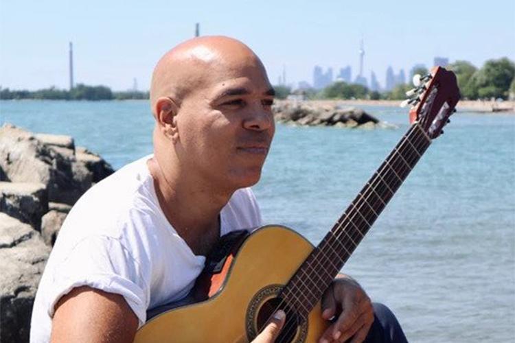 Beau Dixon sits by the Toronto lakeshore, holding a guitar.