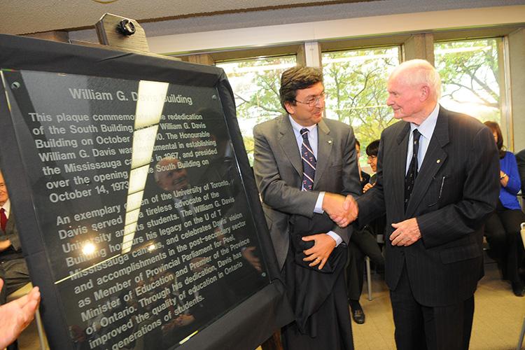 Bill Davis and David Naylor shake hands beside a large plaque with the heading: William G. Davis Building.
