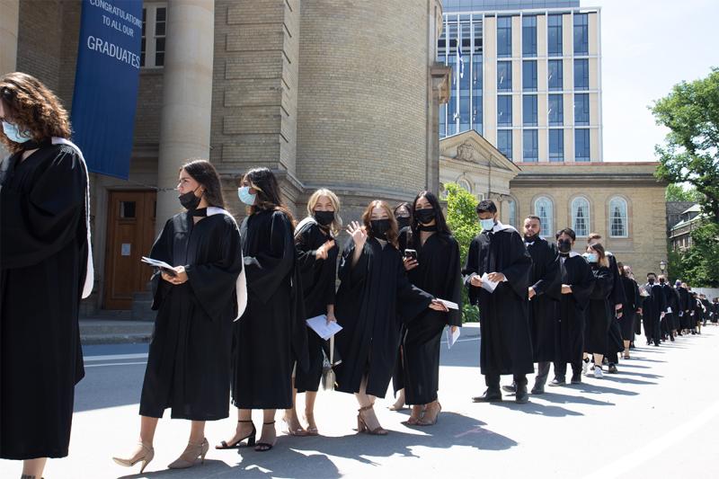 Graduates in gowns and masks wave happily as they line up to enter Convocation Hall.